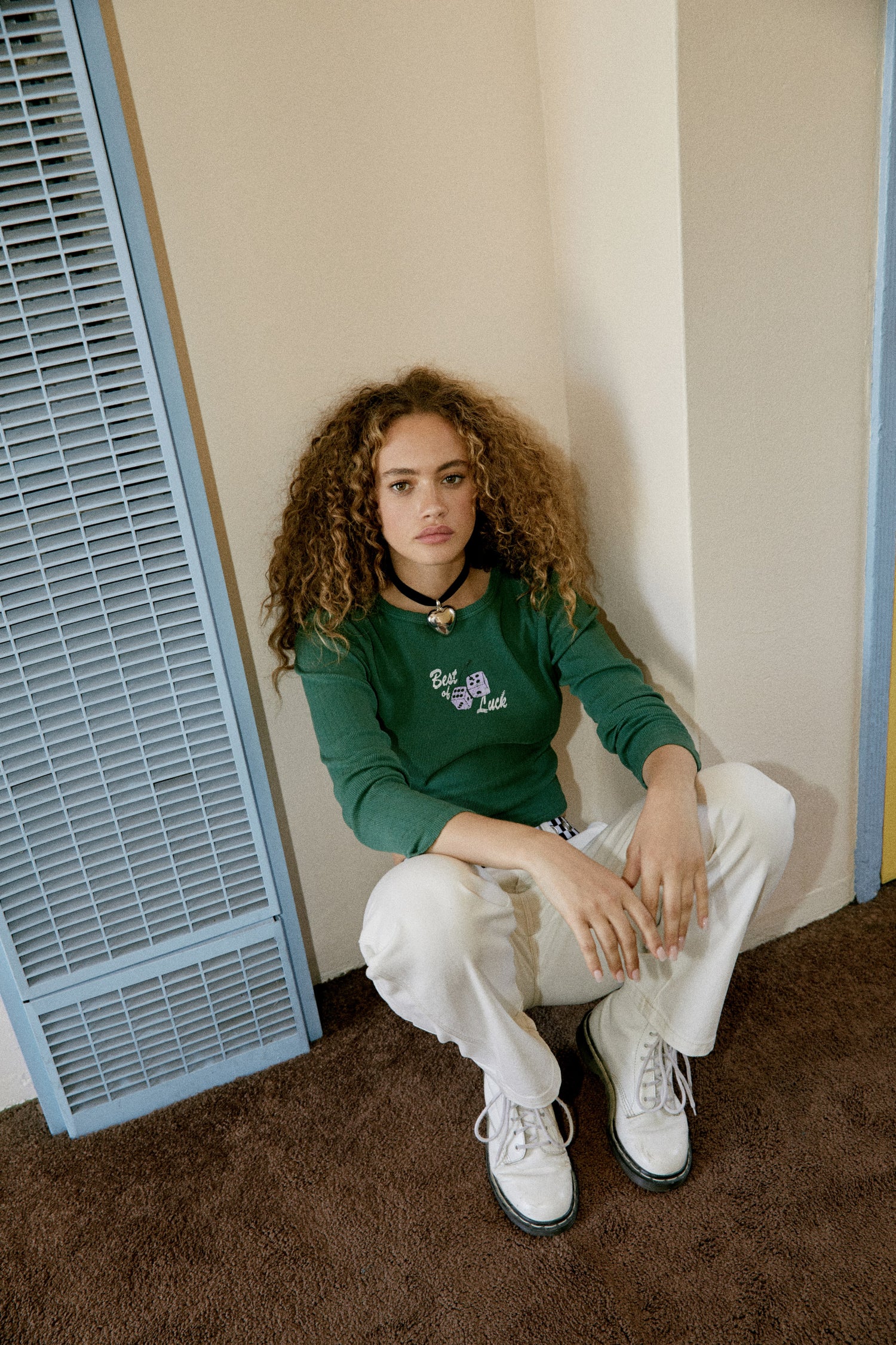 A curly-haired model featuring a storm geen pointelle long sleeve stamped with 'Best of Luck'.