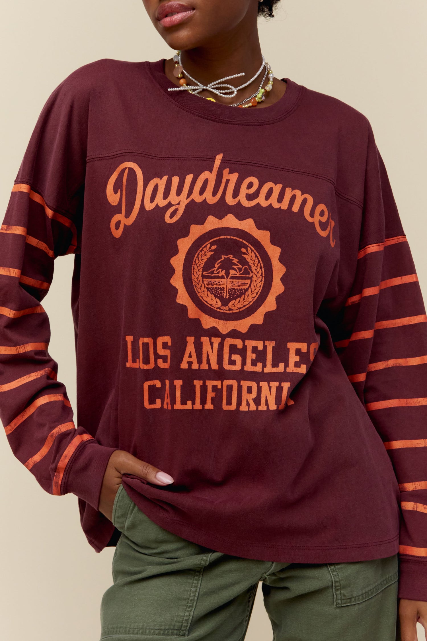 A model featuring a maroon long sleeve stamped with Daydreamer Los Angeles California and orange stripes on the sleeves.