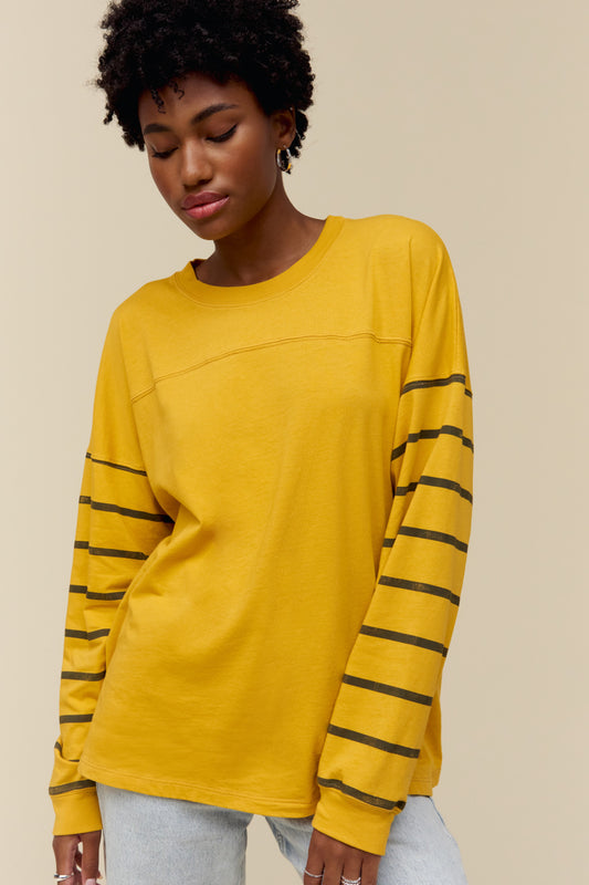 Model wearing a golden-toned long sleeve tee with varsity stripe accents on the arms