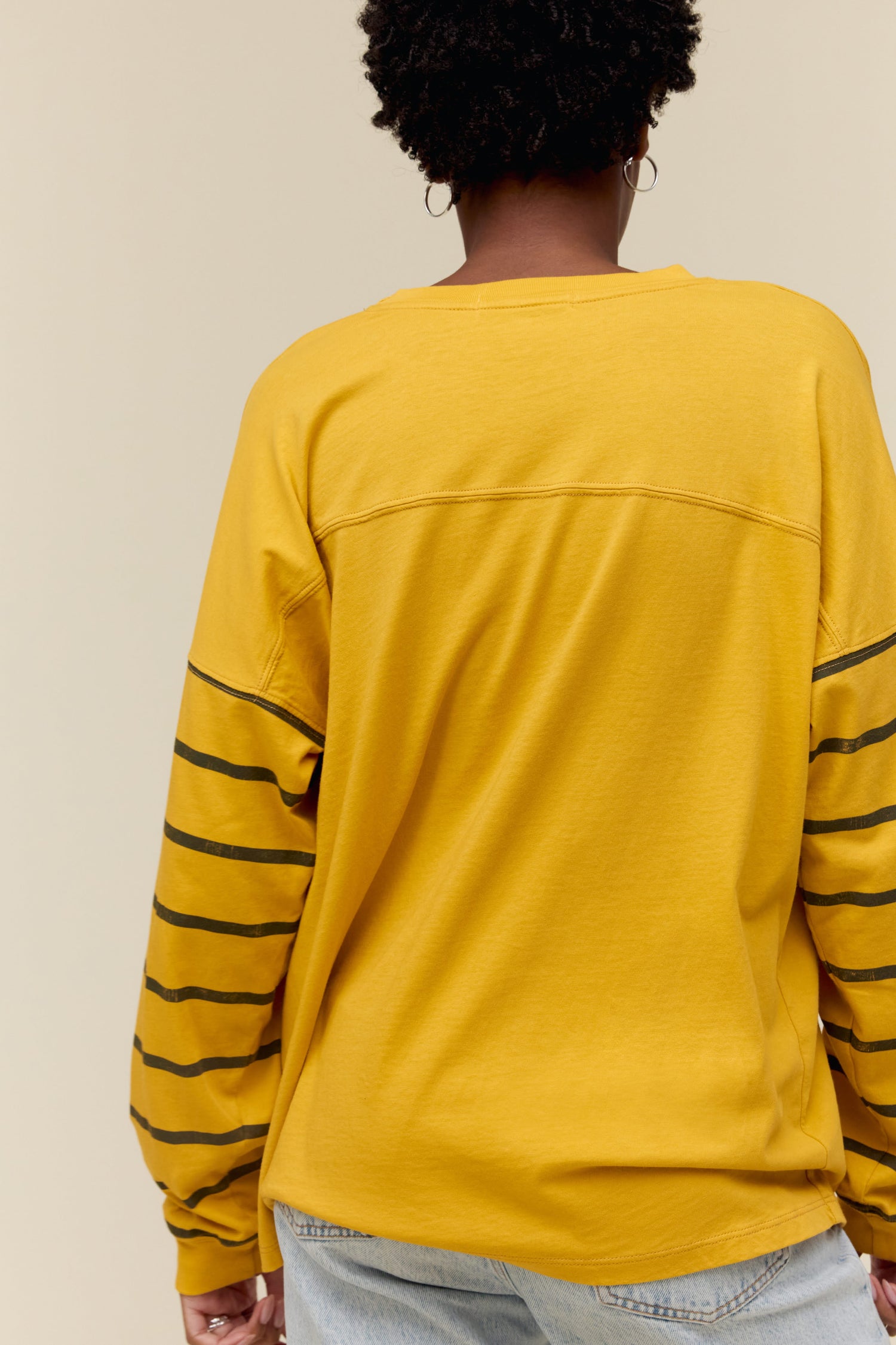 Model wearing a golden-toned long sleeve tee with varsity stripe accents on the arms