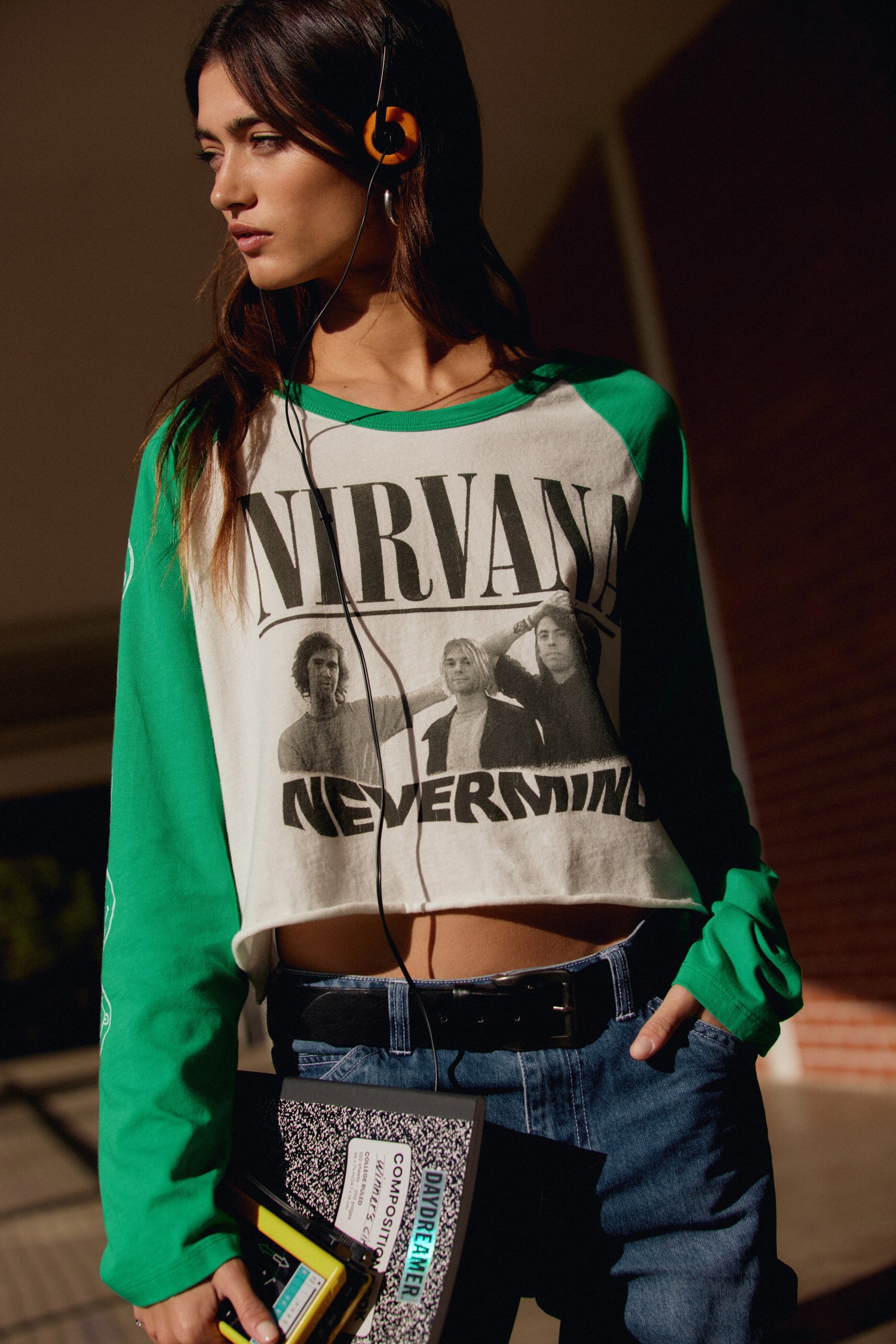 A model featuring a white  crop long sleeve raglan with freen sleeves, stamped with Nirvana and portraits of the band