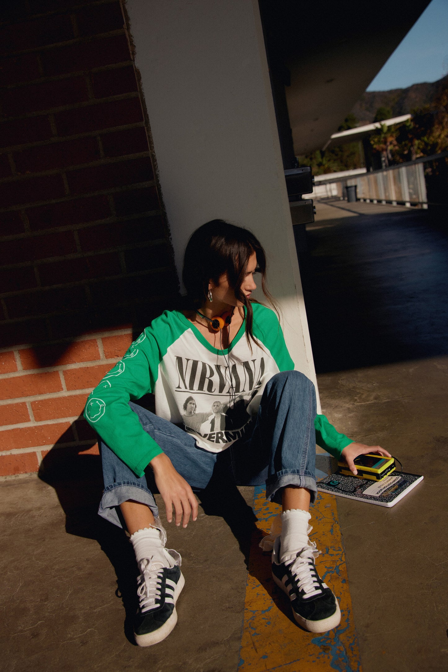 A model featuring a white  crop long sleeve raglan with freen sleeves, stamped with Nirvana and portraits of the band