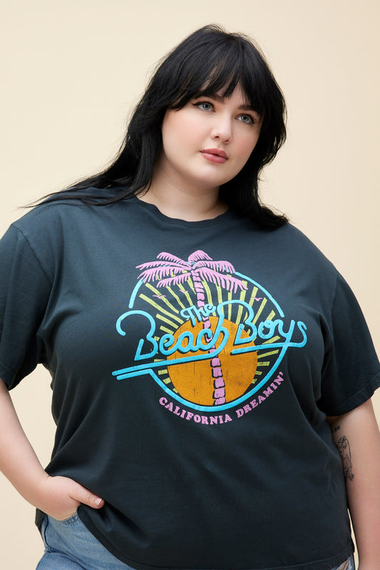 Plus size model wearing a black boyfriend tee with a neon graphic of The Beach Boys in front of a sun and palm tree. 
