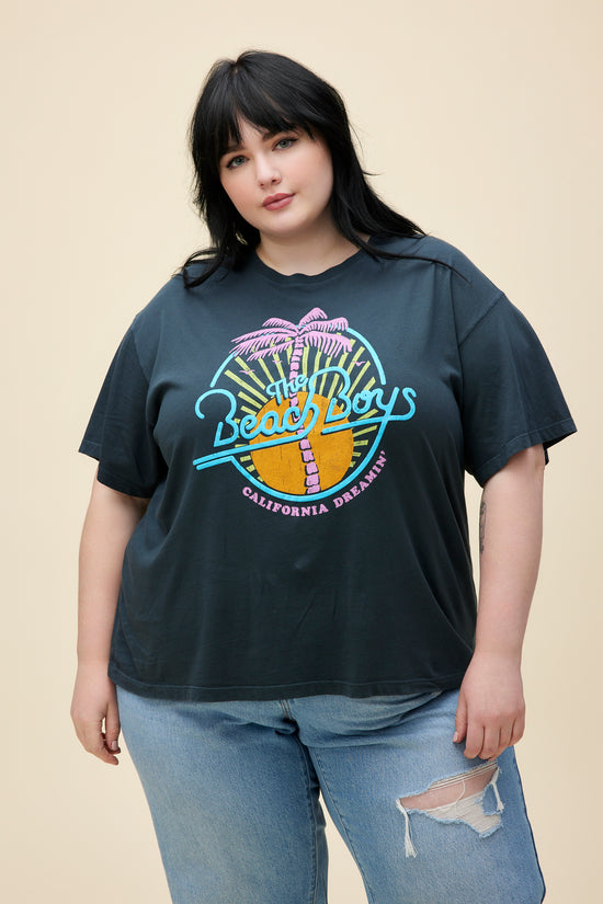 Plus size model wearing a black boyfriend tee with a neon graphic of The Beach Boys in front of a sun and palm tree. 