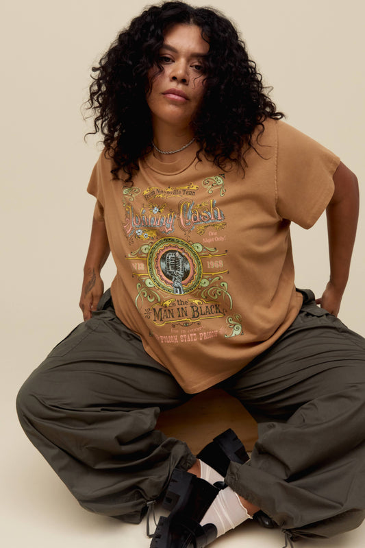 A model featuring a hazelnut colored Johnny Cash es gf tee stamped with "Man in Black" and a microphone label placing spotlight on “Johnny Cash at Folsom Prison”.