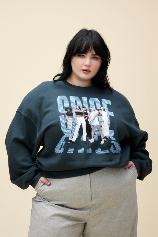 A  plus size model wearing black sweatshirt featuring a large font "SPICE GIRLS" and a portrait of the group. 
