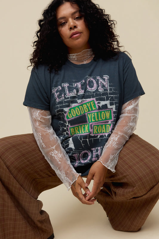 A model featuring a vintage black oversized tee featuring motifs from Elton John's Goodbye, Yellow Brick Road album's original cover, designed with a brick road graphic and accented with rhinestones.
