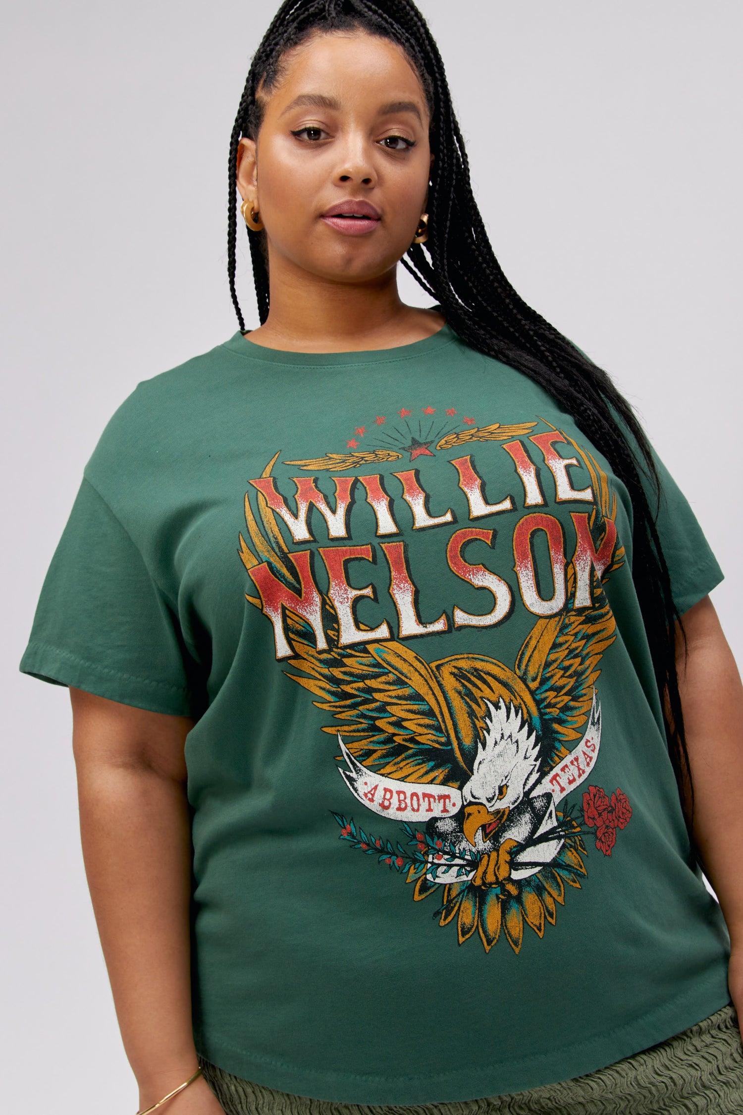 A dark-haired model featuring a green tee stamped with 'Willie Nelson' and designed with a bird with 'Abott Texas' on its mouth.