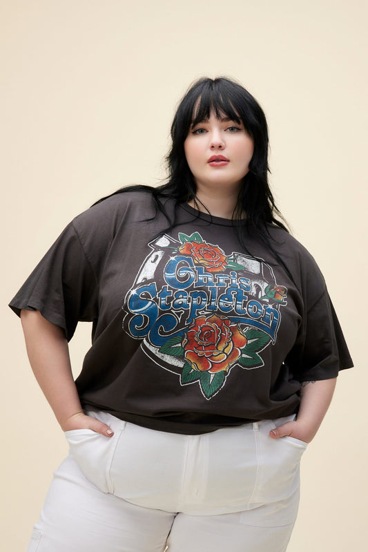 A plus size model featuring a black merch tee stamped with 'Chris Stapleton' in the middle with flowers around.