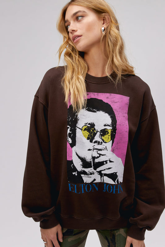 A blonde-haired model featuring a dark brown bf crew stamped with 'Elton John' and designed with an iconic portrait of the artist.