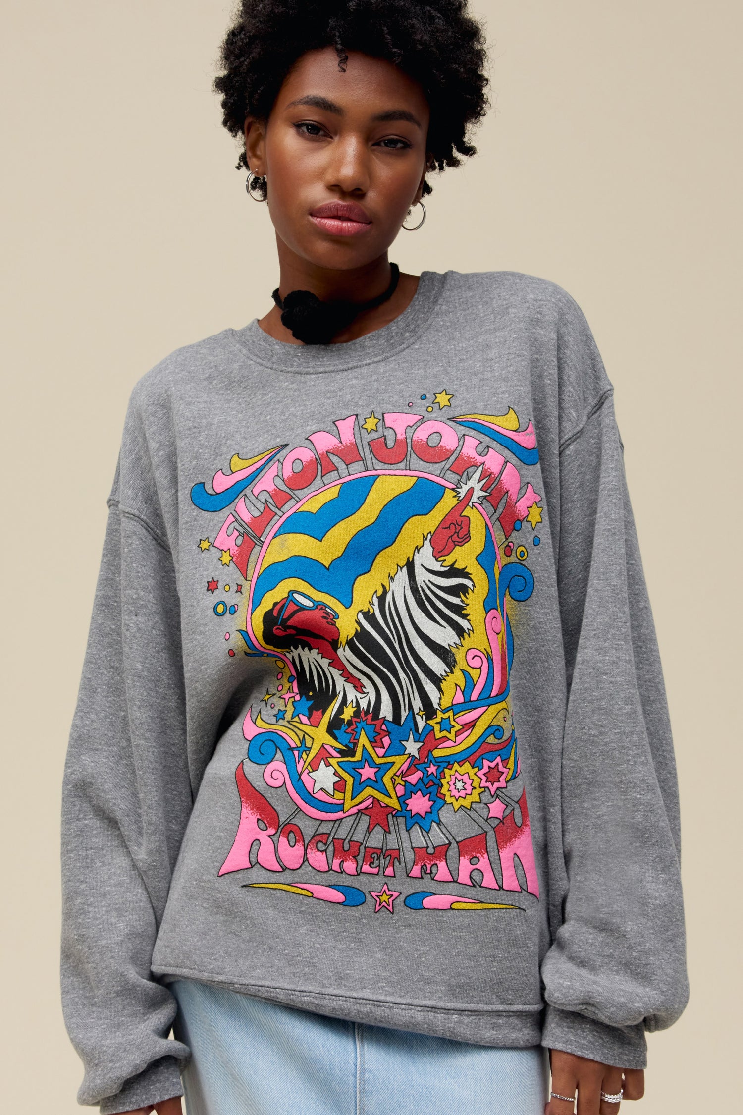 A model featuring a gray long sleeve stamped with Elton John and a graphic of a man and stars.
