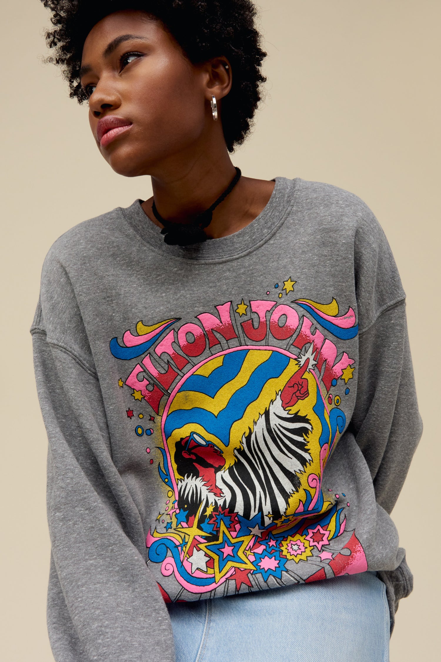 A model featuring a gray long sleeve stamped with Elton John and a graphic of a man and stars.