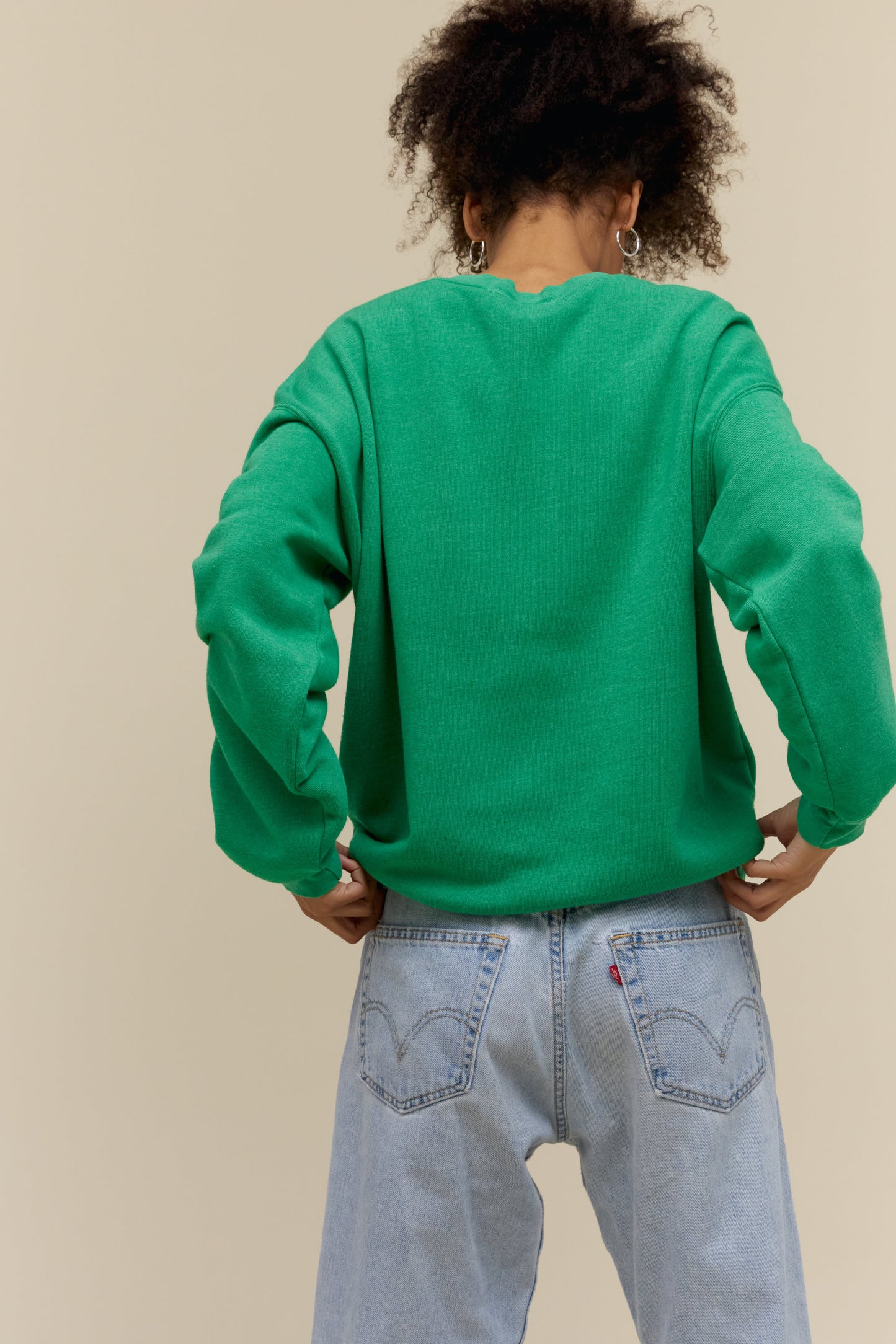 Curly-haired model wearing an oversized tri-blend fleece sweatshirt in green with contrast orange 'Tokyo' collegiate style lettering
