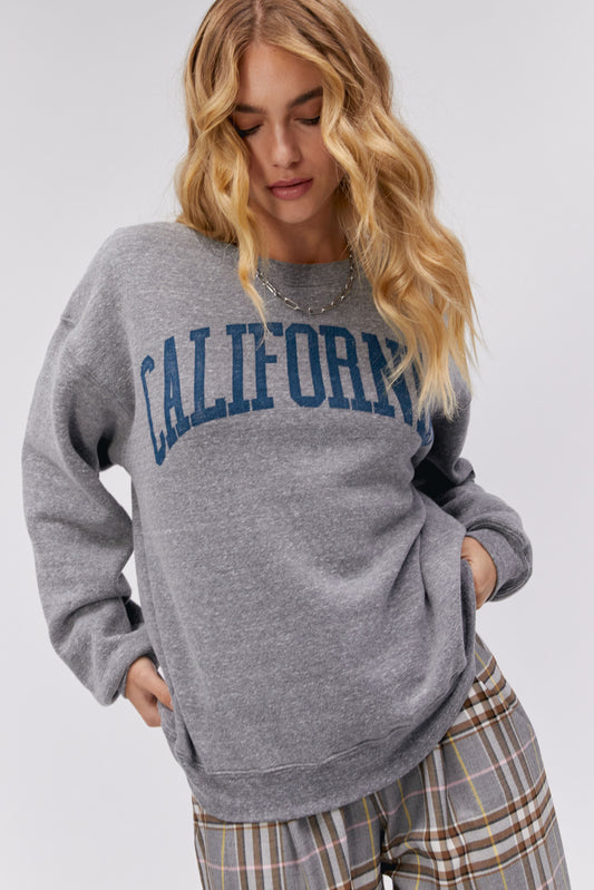 A blonde curly-haired model featuring a grey boyfriend crew stamped with 'California' in collegiate style letters.