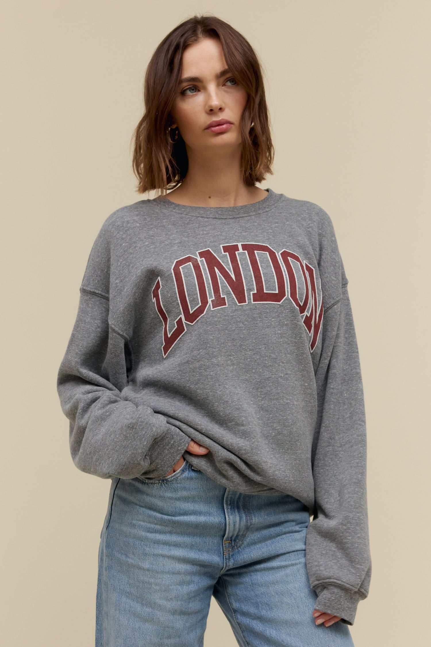 Short-haired model wearing an oversized tri-blend fleece sweatshirt in heather grey with contrast maroon 'London' collegiate style lettering