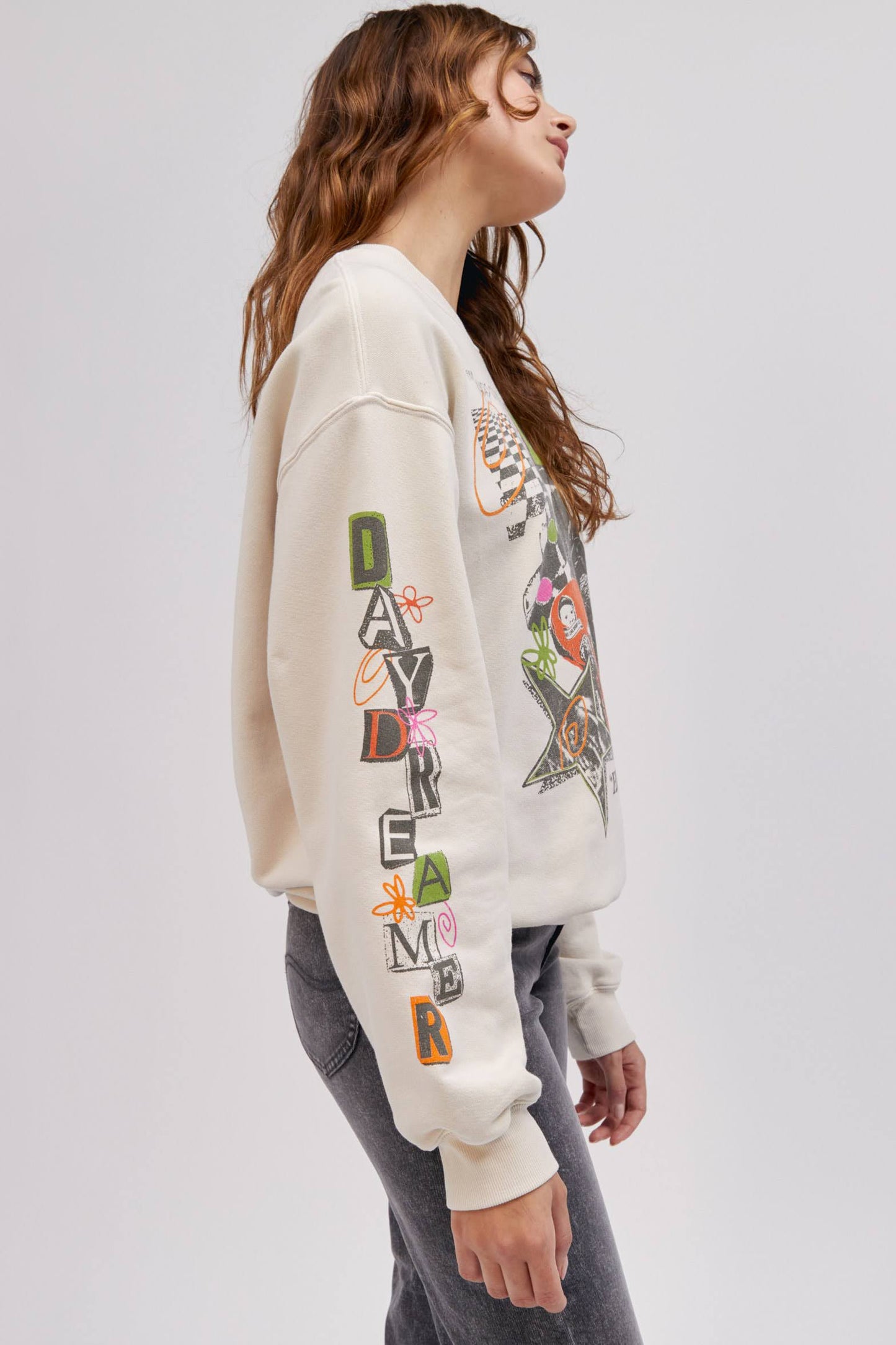 side profile pose of model wearing off white colored sweatshirt with graphics on the sleeve