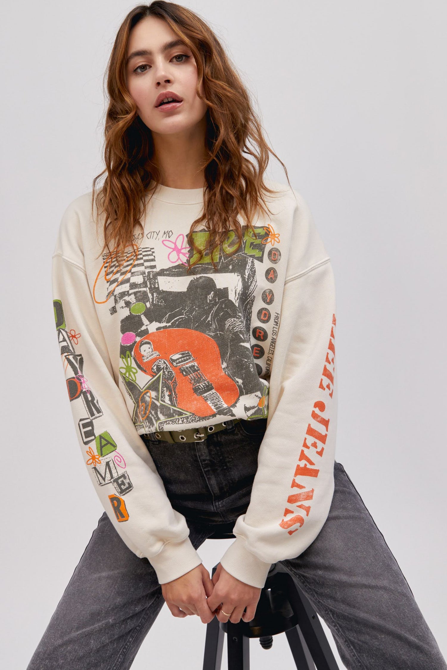 model in sitting pose wearing an off white colored graphics sweatshirt and washed denim jeans