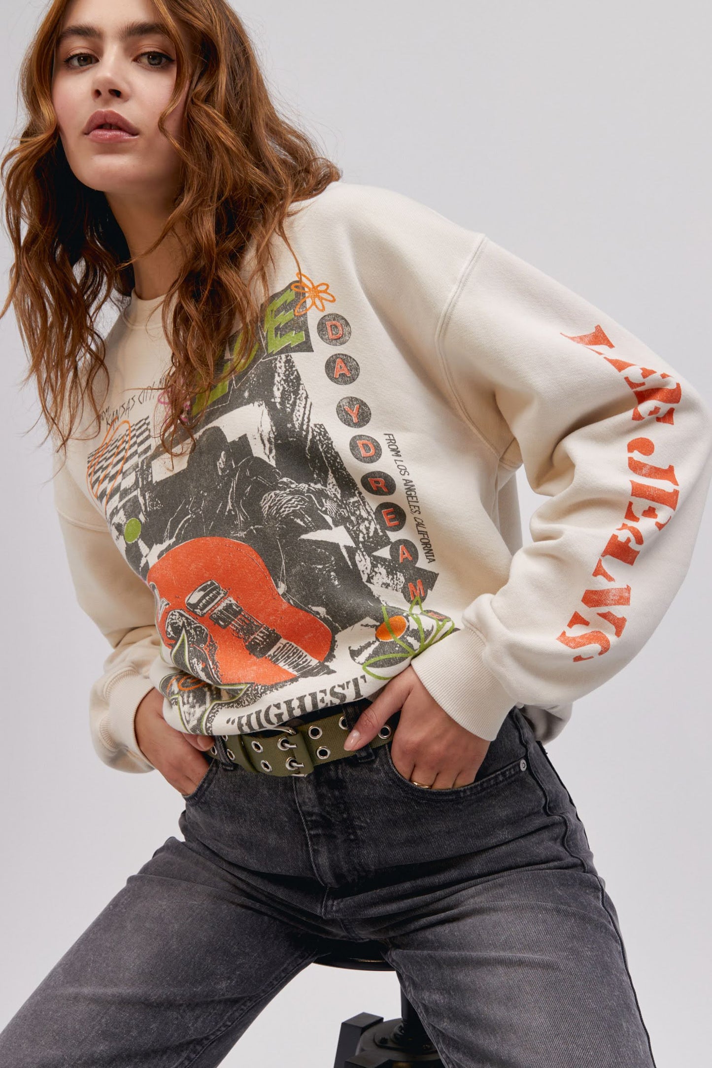 long haired model in sitting pose with hands in pockets wearing a washed graphic sweatshirt