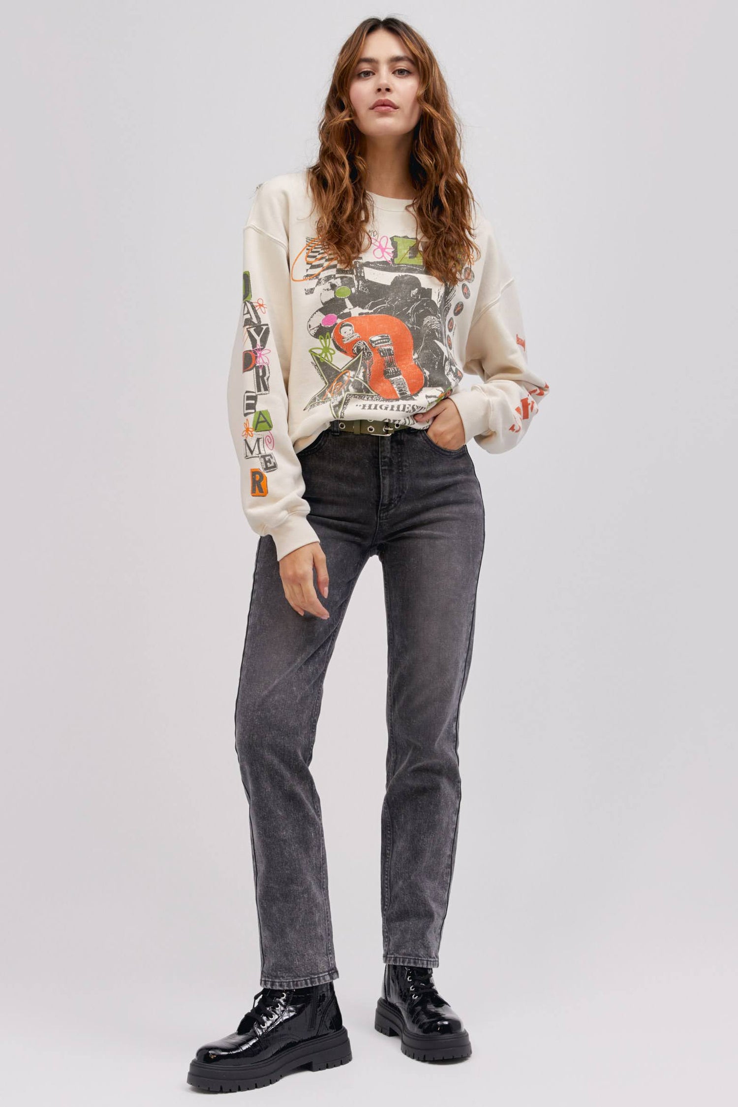 model in standing pose with hand in pocket wearing a graphic sweatshirt and washed denim jeans