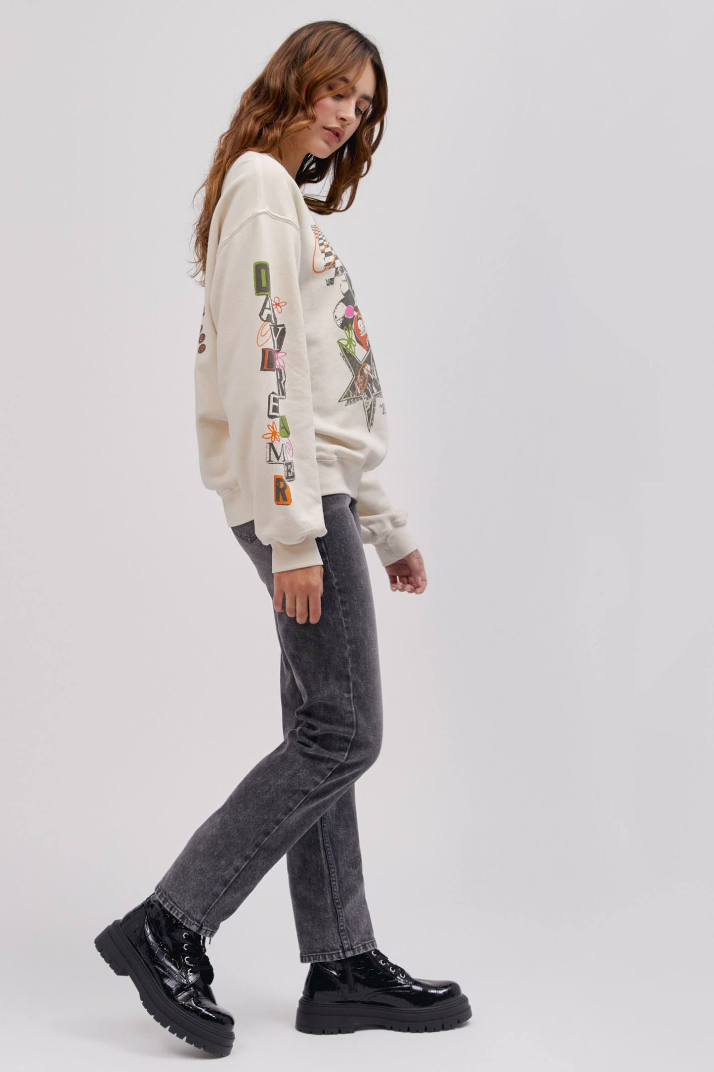 side profile pose of model wearing graphic sweatshirt and washed denim jeans