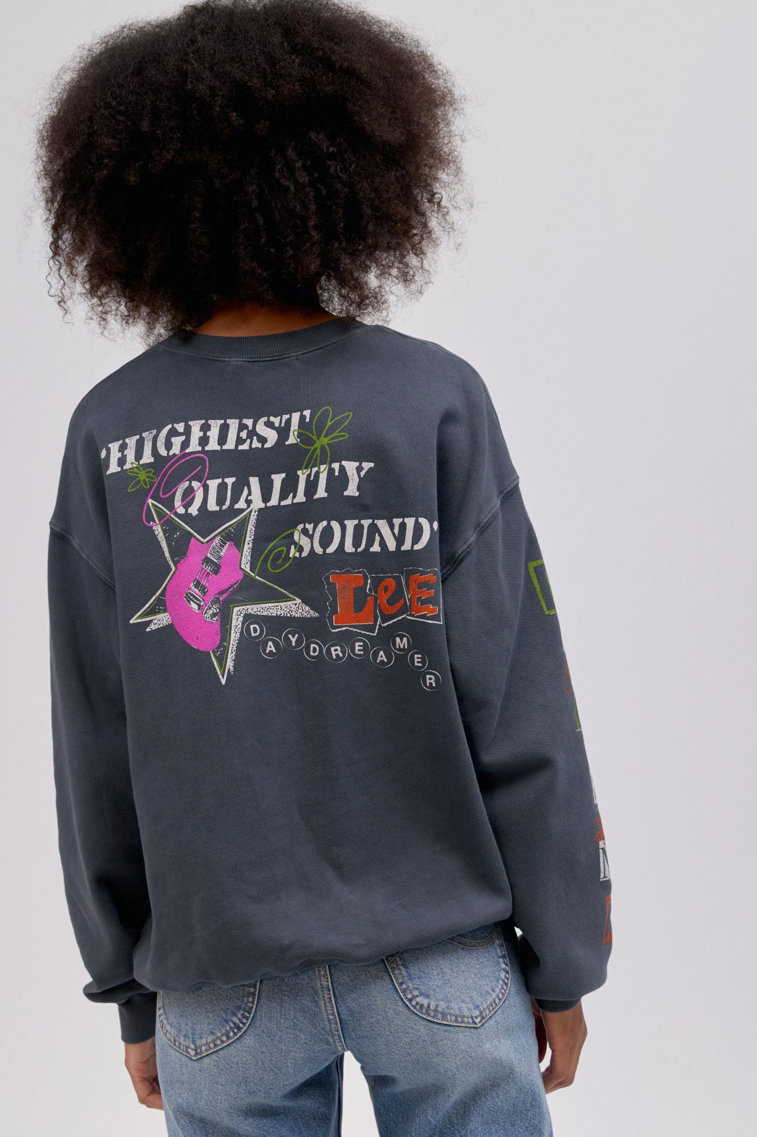 Backside of curly haired model wearing a Lee x Daydreamer collab graphic sweatshirt in washed black.