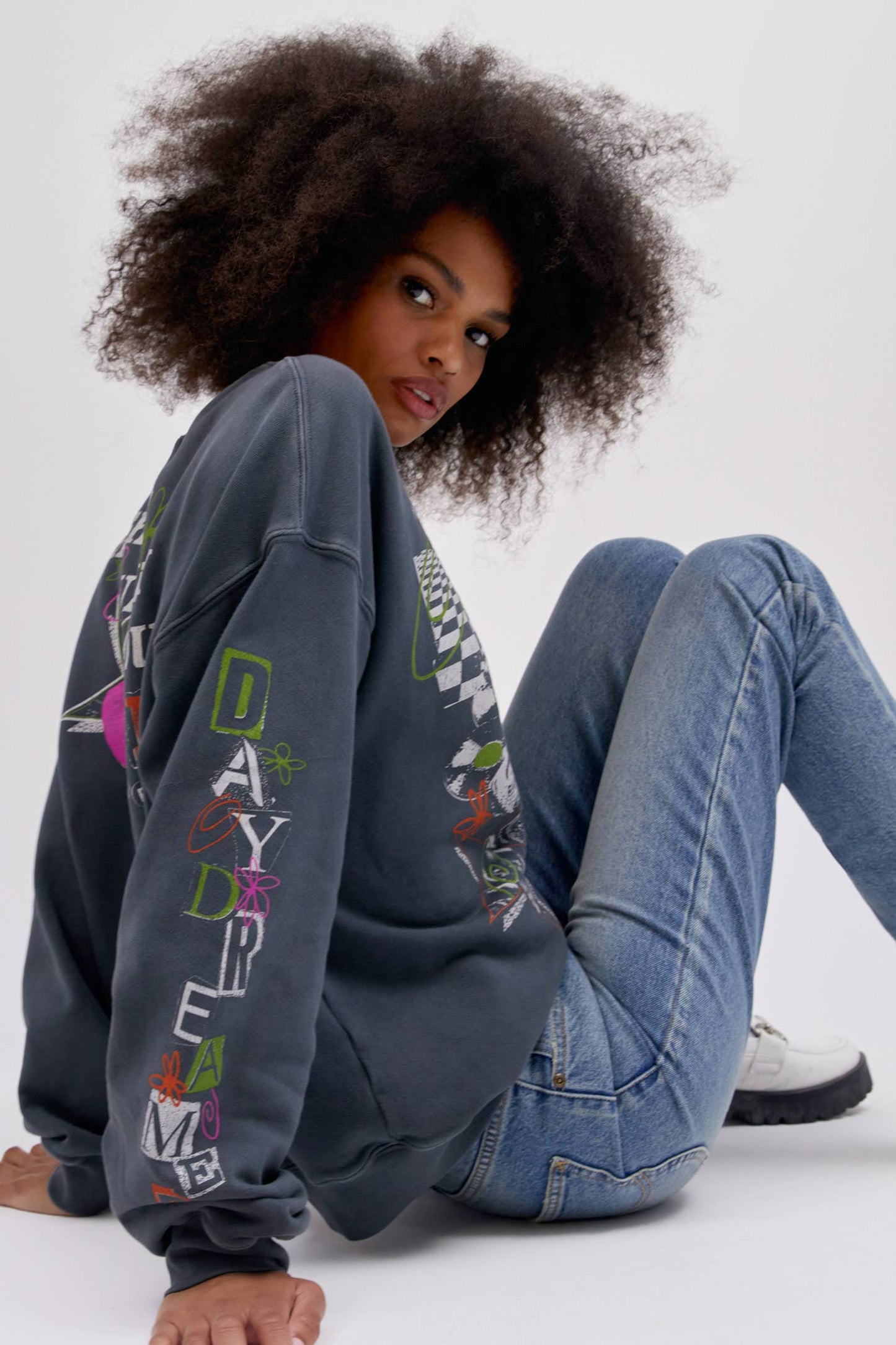Backside of sitting curly haired model wearing a Lee x Daydreamer collab graphic sweatshirt in washed black.