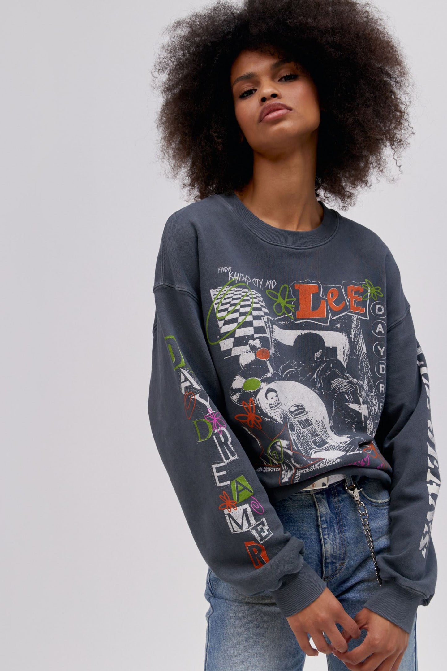 Curly haired model wearing a Lee x Daydreamer collab graphic sweatshirt in washed black.