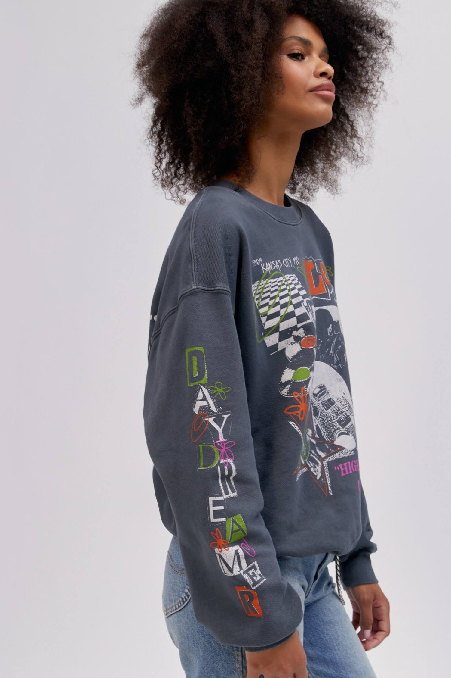 Side profile of curly haired model wearing a Lee x Daydreamer collab graphic sweatshirt in washed black.
