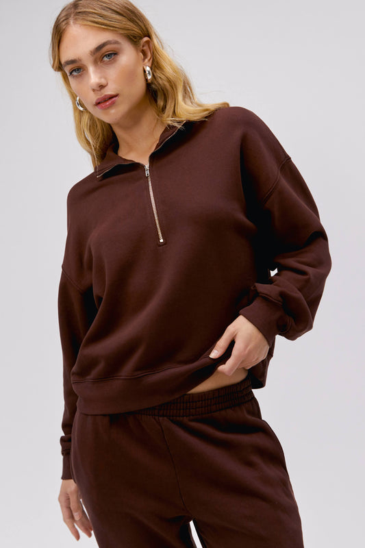 Model wearing a solid half zip sweatshirt in dark auburn.
