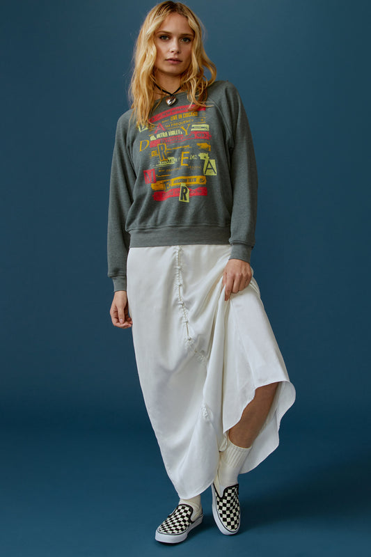 A blonde-haired model featuring a grey crew sweatshirt stamped with 'Daydreamer' graphics all over the front.