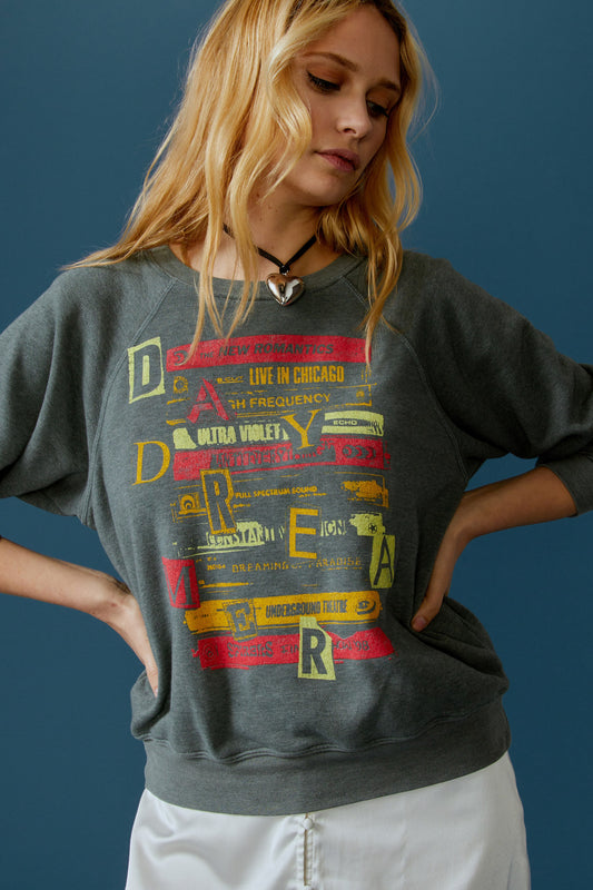 A blonde-haired model featuring a grey crew sweatshirt stamped with 'Daydreamer' graphics all over the front.