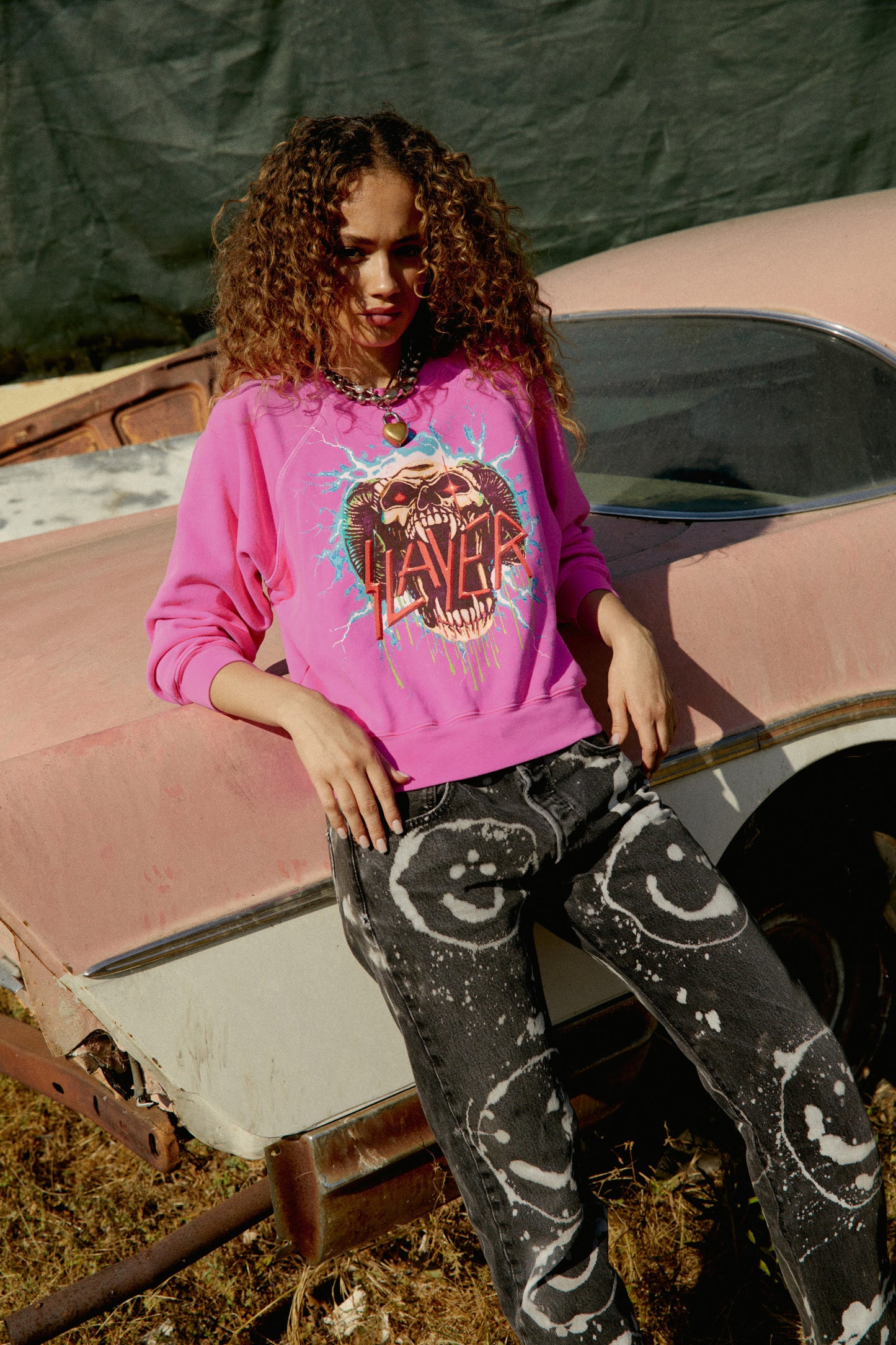 Model wearing Slayer graphic sweatshirt in pink with lightning artwork.