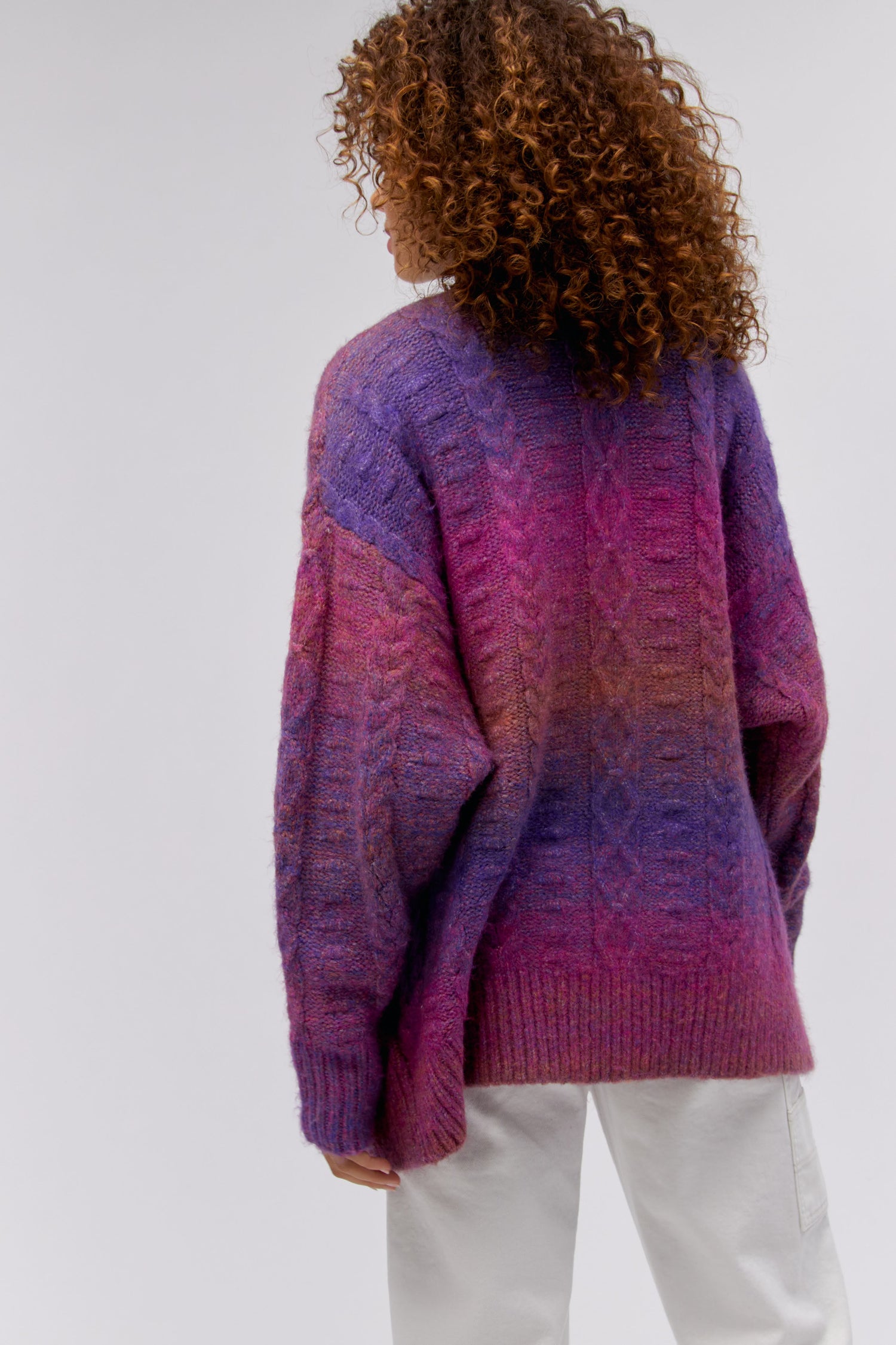 A curly-haired model featuring an ombre cardigan in Wild Orchid.