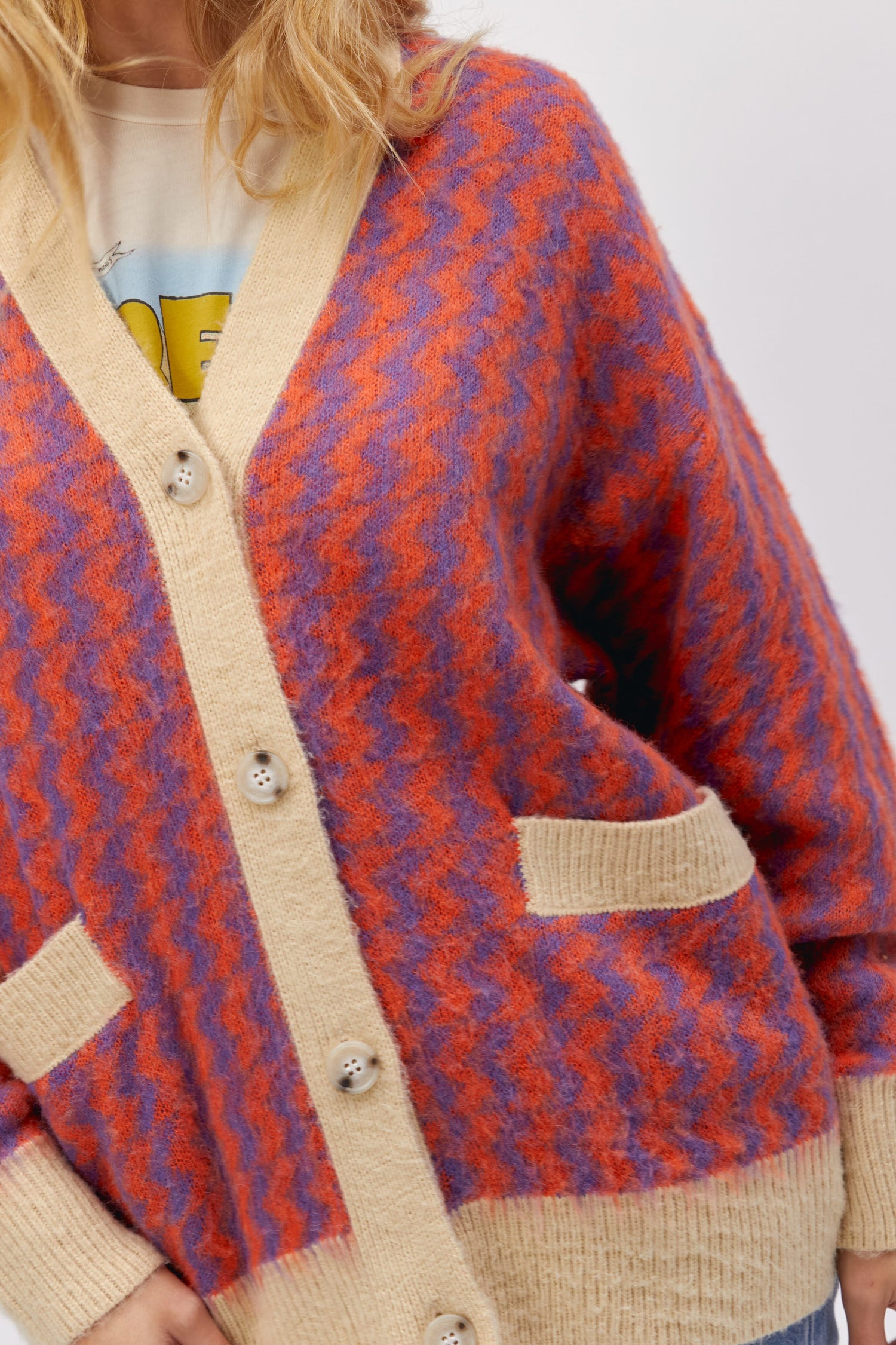 A blonde-haired model featuring a violet orange zig zag cardigan.