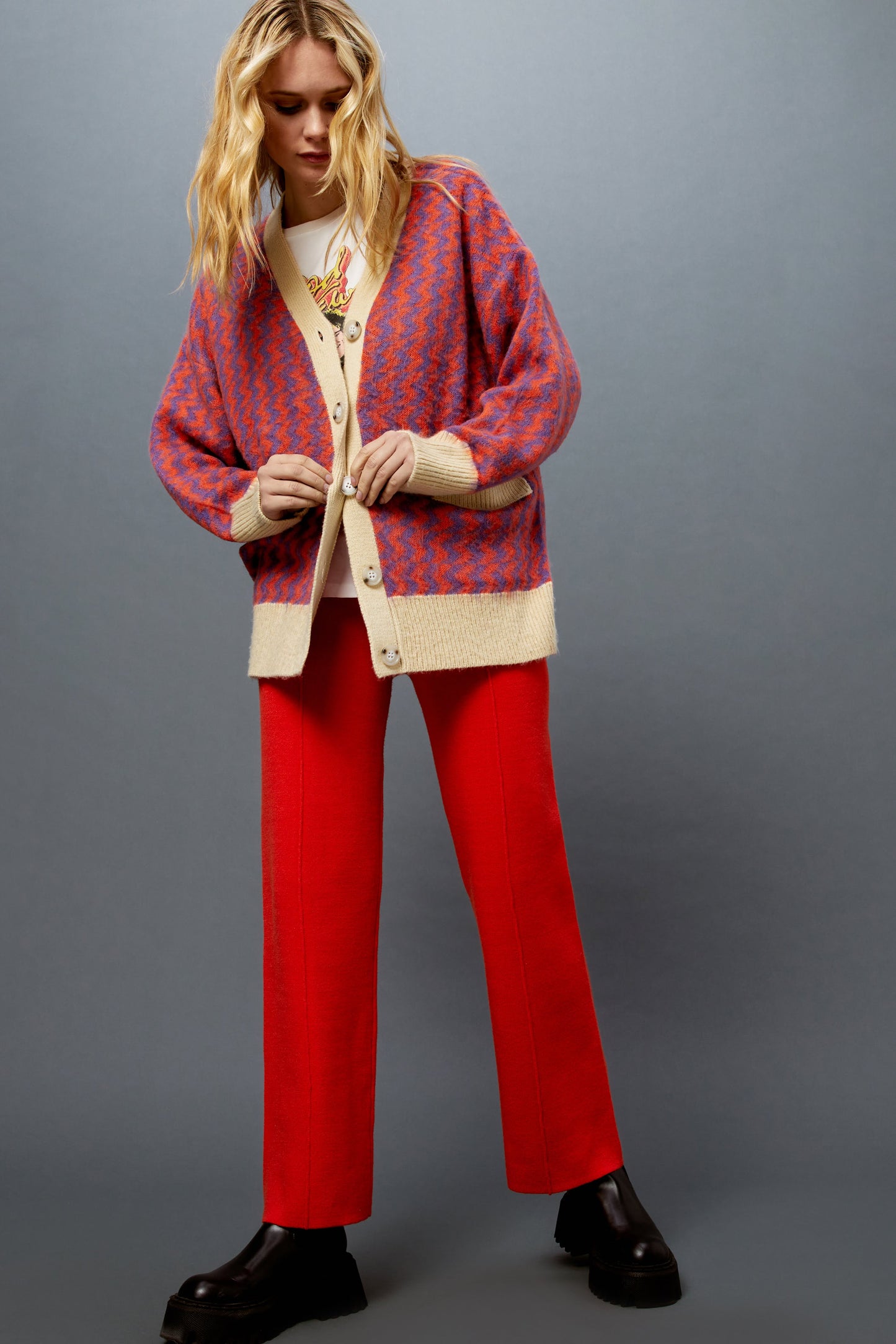 Model wearing a zig zag pattern cardigan styled with a Rod Stewart graphic tee and hot orange knit pintuck pants