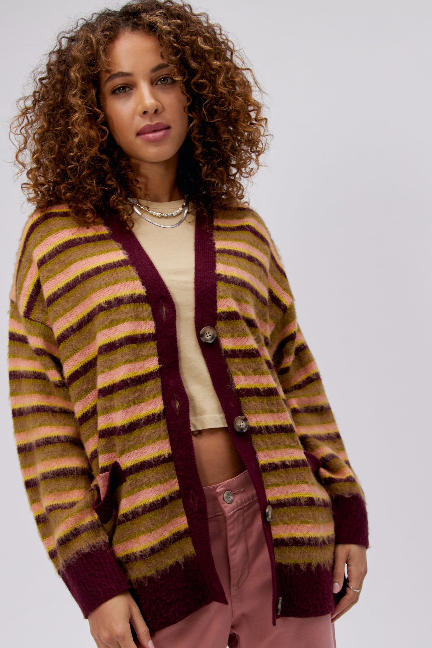A curly-haired model featuring a cherry crush stripe cardigan.