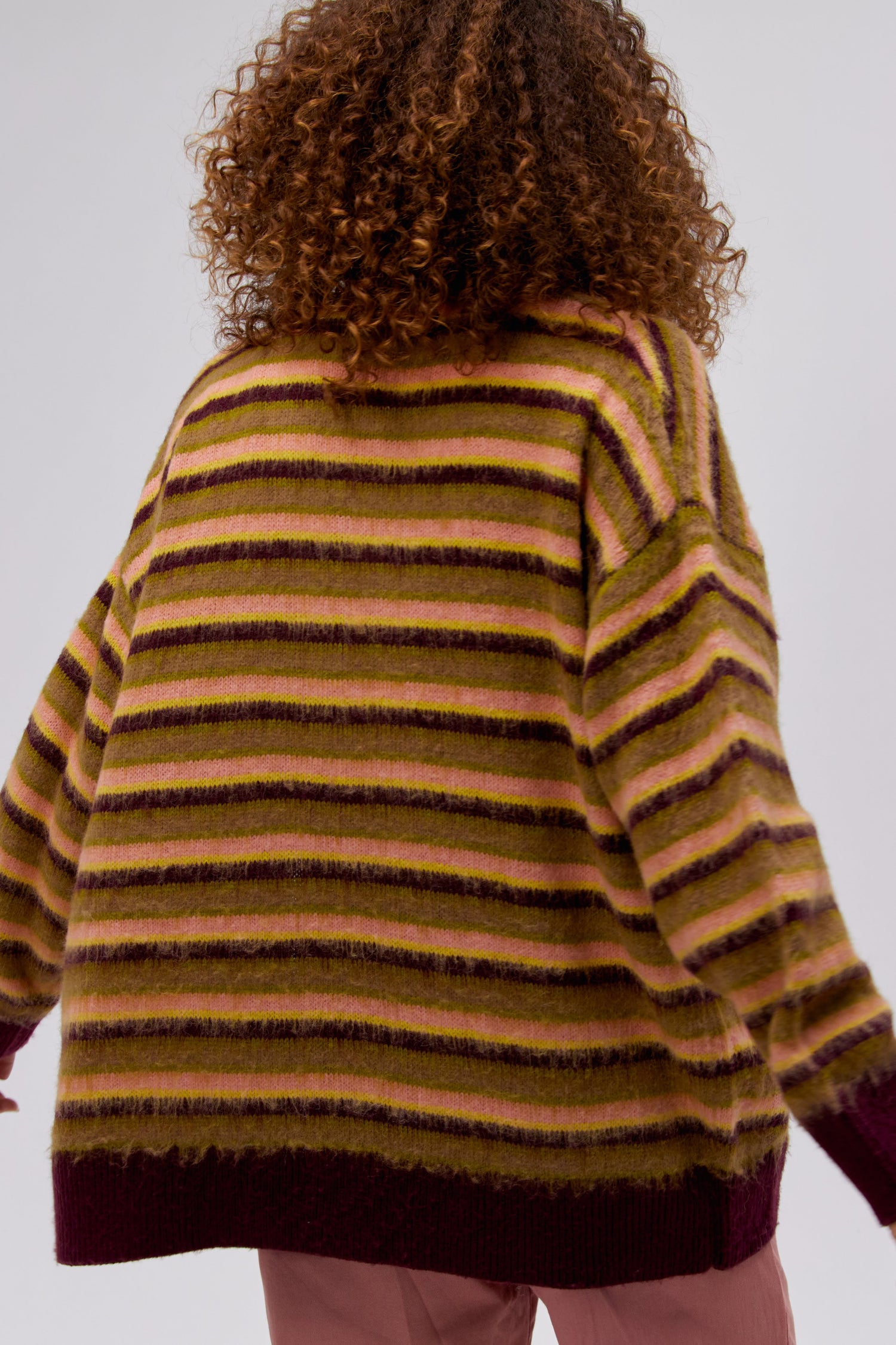 A curly-haired model featuring a cherry crush stripe cardigan.