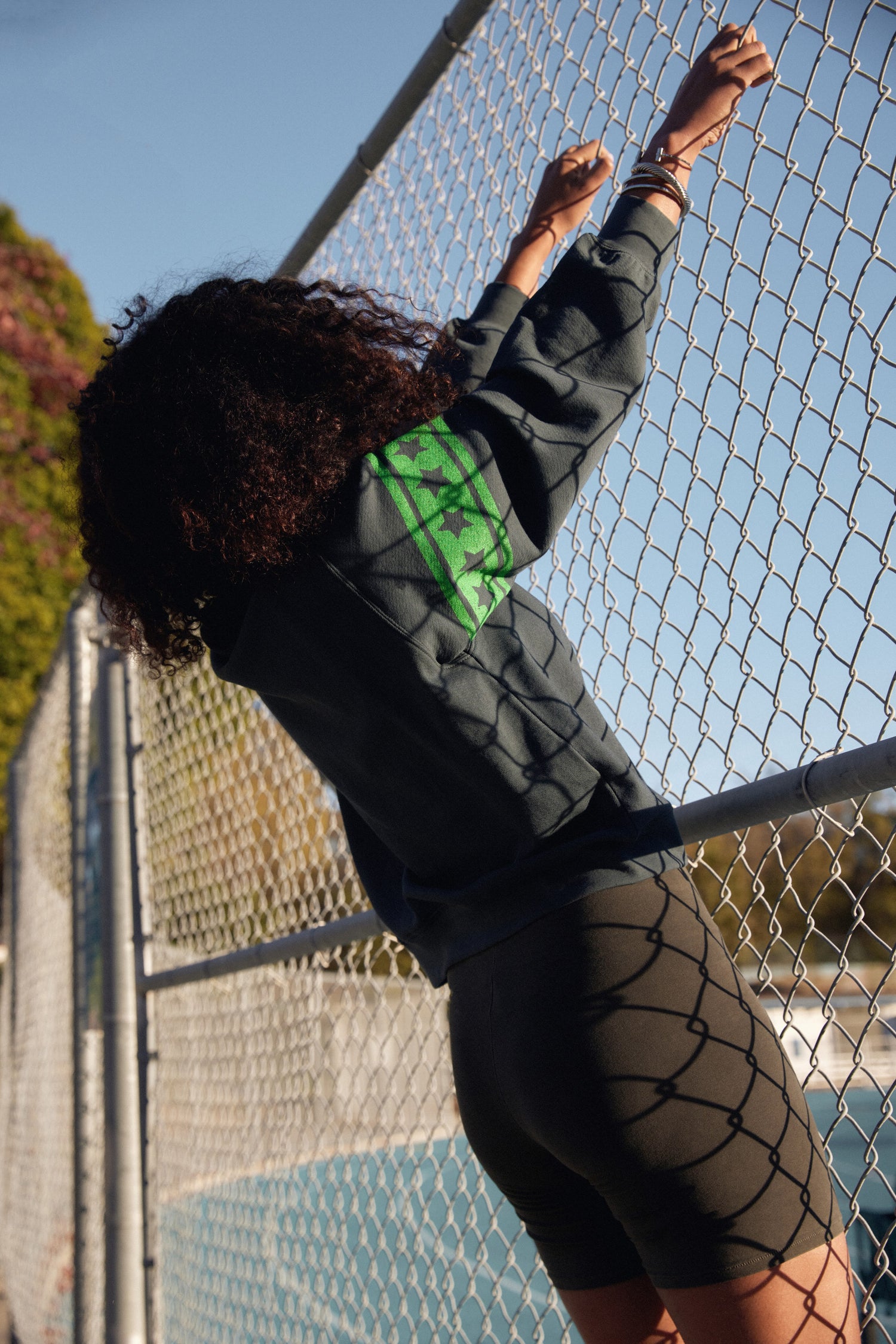 A model featuring a black sweatshirt designed with a  large star in the middle, stamped with "Lucky Star" and green stripes on the sleeves.