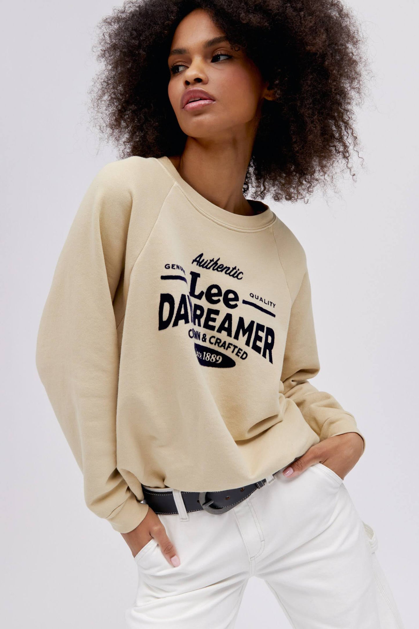 curly haired model posing with hands in pockets wearing a khaki colored sweatshirt