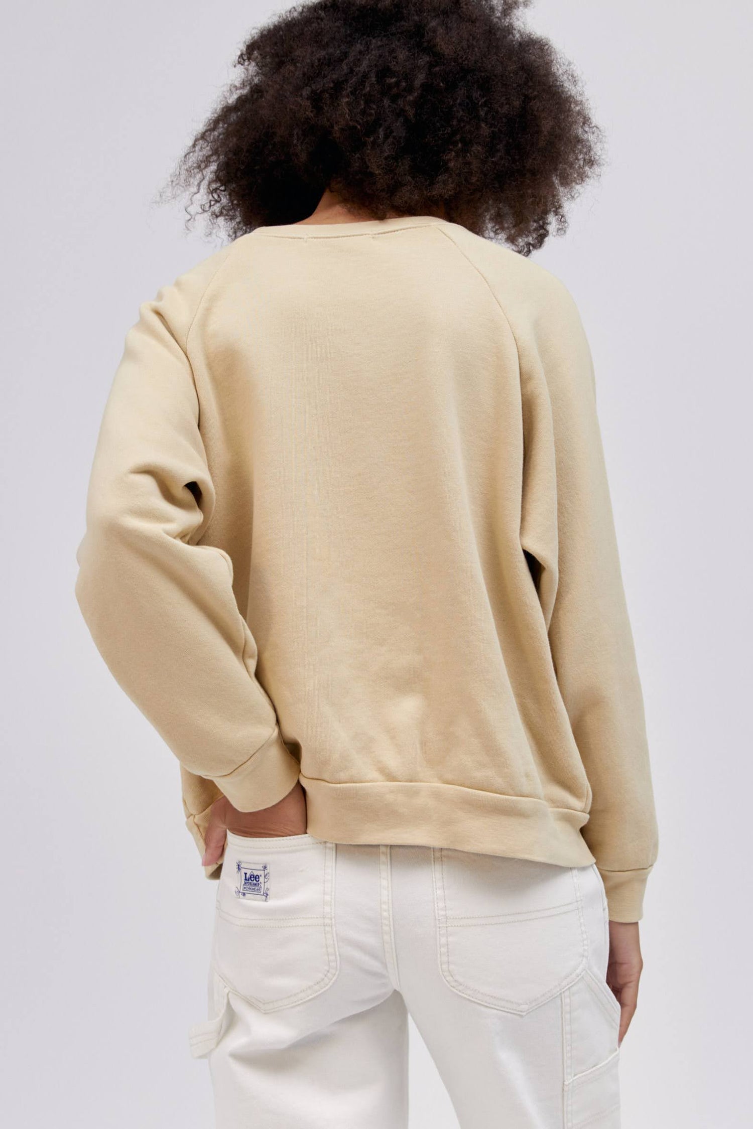backside of curly haired model with hand in back left pocket wearing a khaki colored sweatshirt