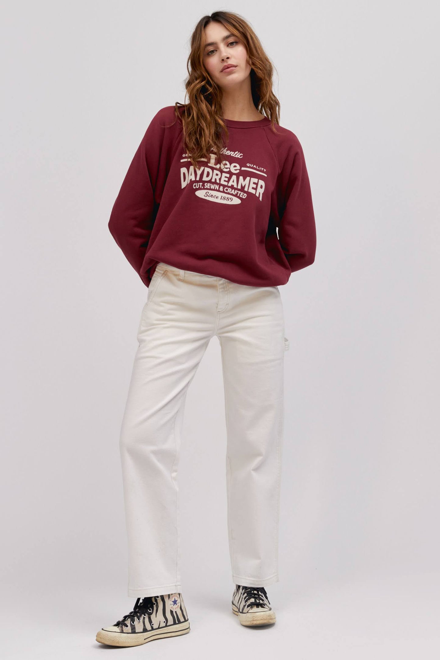 long wavy haired model in standing pose wearing maroon colored sweatshirt and white workwear pants