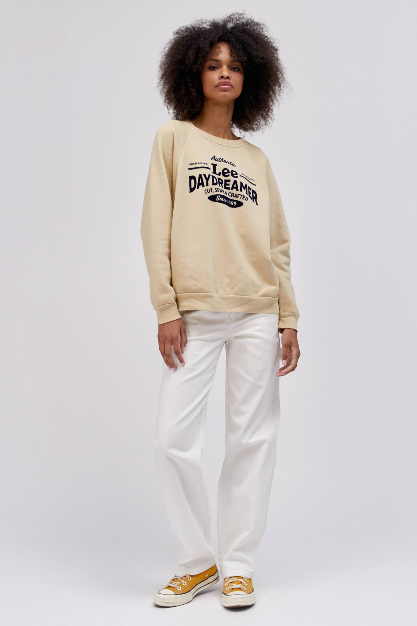 curly haired model wearing khaki colored sweatshirt and white workwear pants