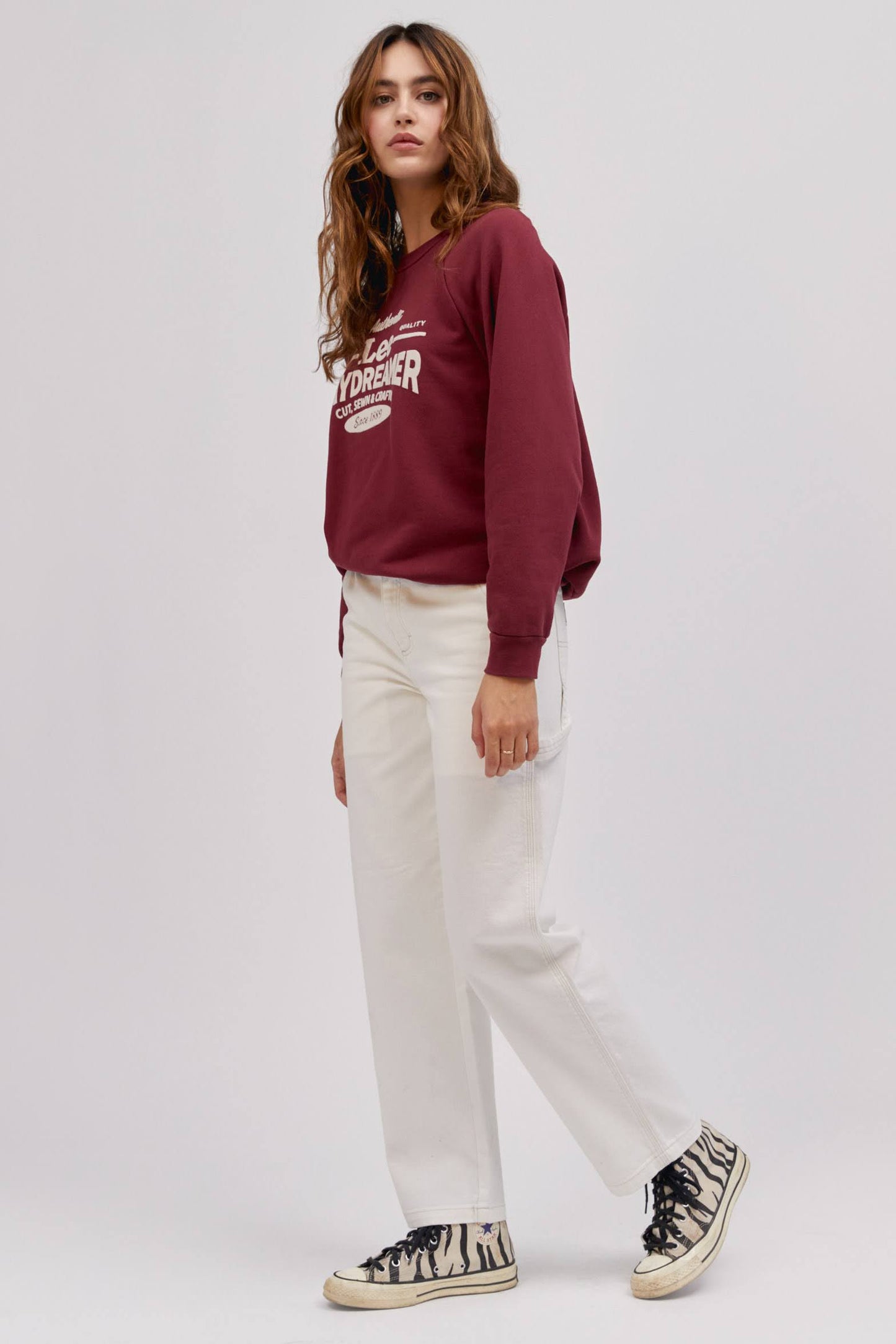 long wavy haired model in side standing pose wearing maroon colored sweatshirt and white workwear pants