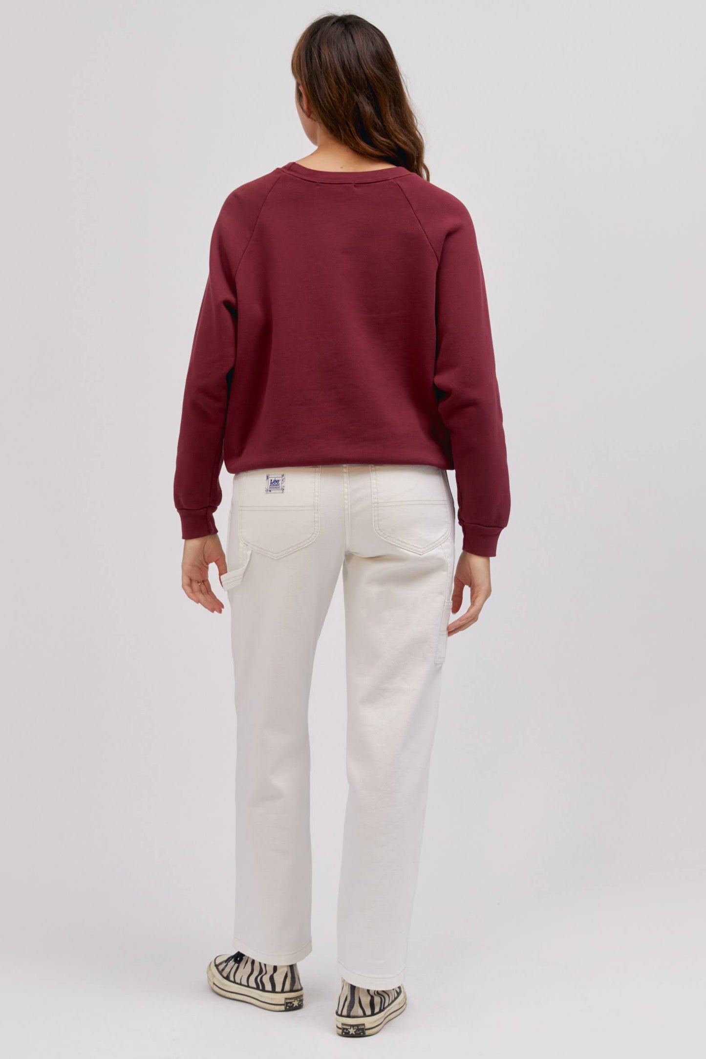 backside of standing model wearing maroon colored sweatshirt and white workwear pants
