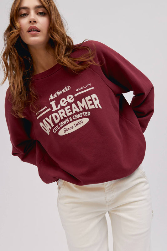 long wavy haired model posing while wearing maroon colored sweatshirt with flocked logo graphics