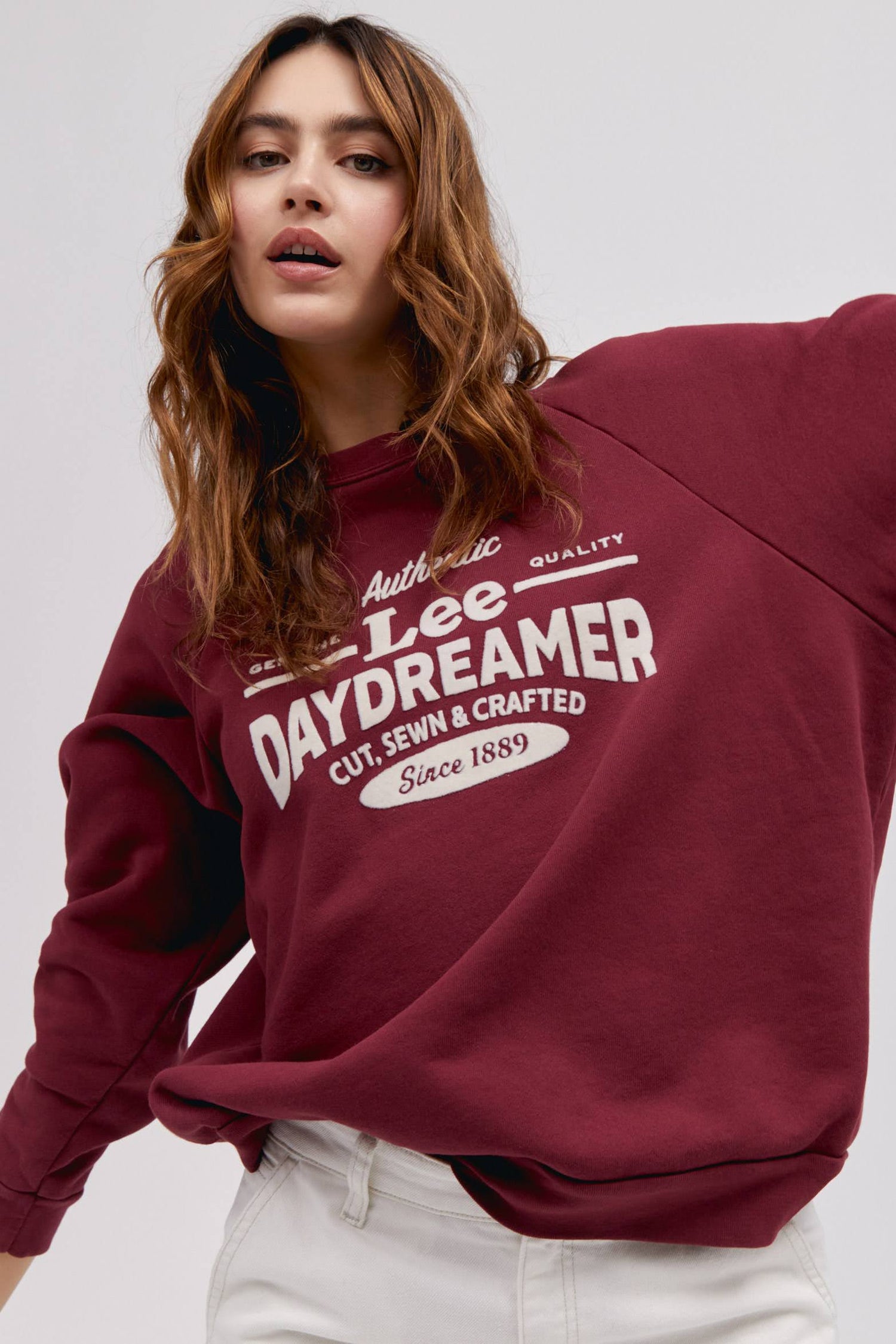 long wavy haired model posing while wearing maroon colored sweatshirt with flocked logo graphics