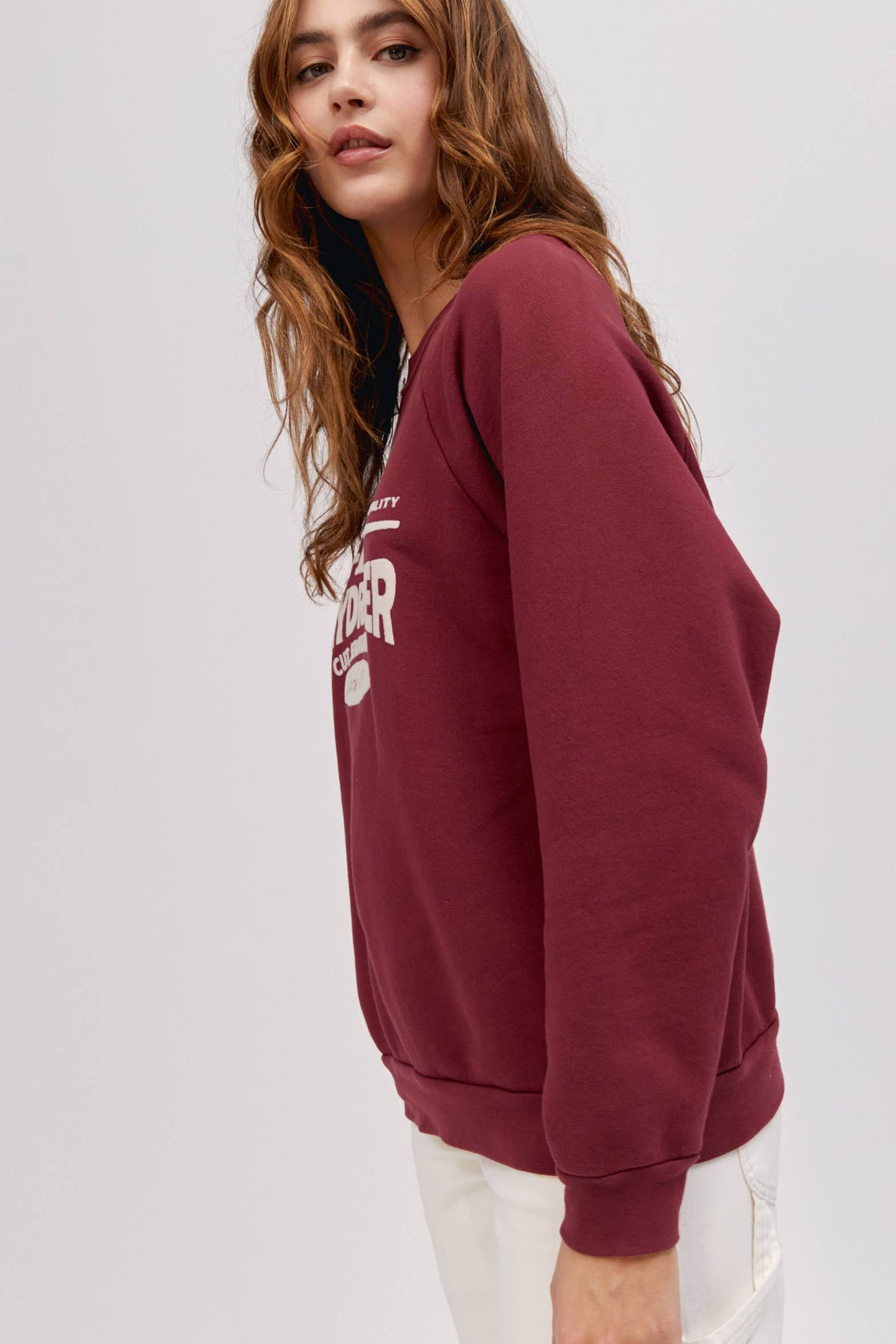 long wavy haired model posing to the side wearing maroon colored sweatshirt