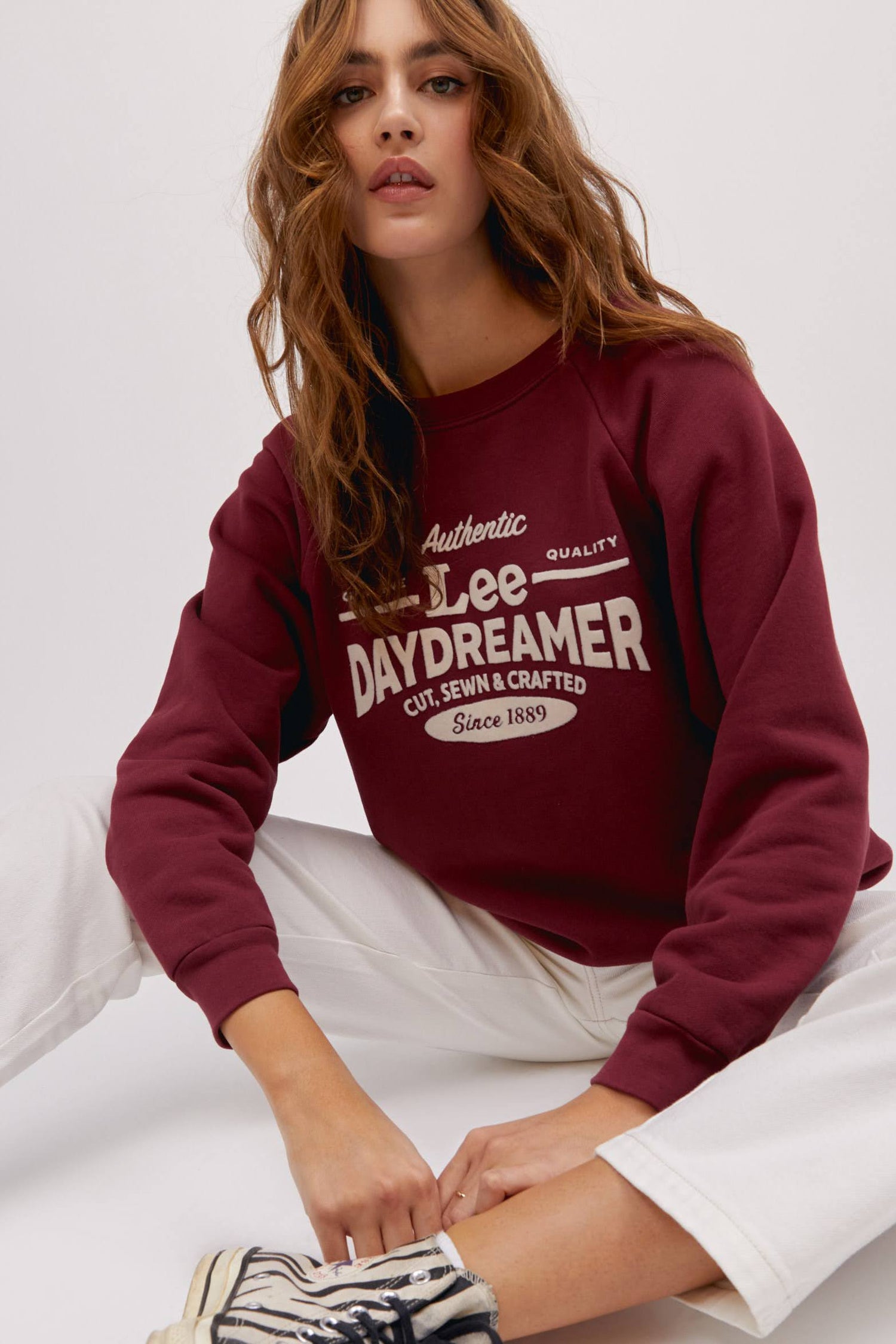 long wavy haired model in sitting pose wearing maroon colored sweatshirt and white workwear pants
