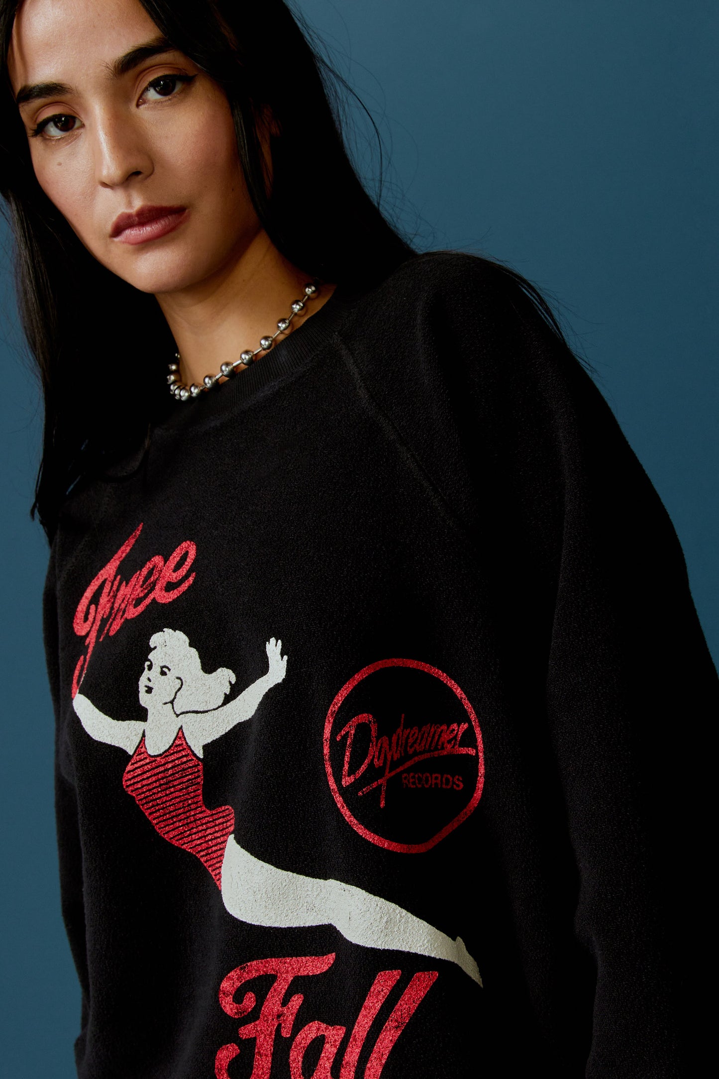 A dark-haired model featuring a black long sleeve stamped with 'Free Fall' in red font and a graphic of a falling girl in a red one-piece.