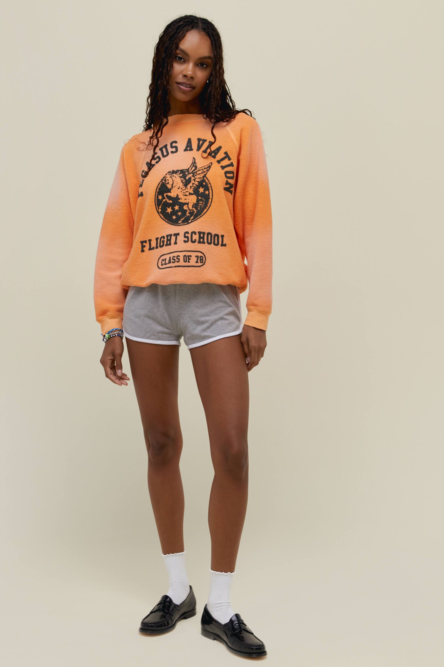 A model featuring a soft peach raglan crew stamped with "Pegasus Aviation Flight School" and a graphic of a pegasus on the center.